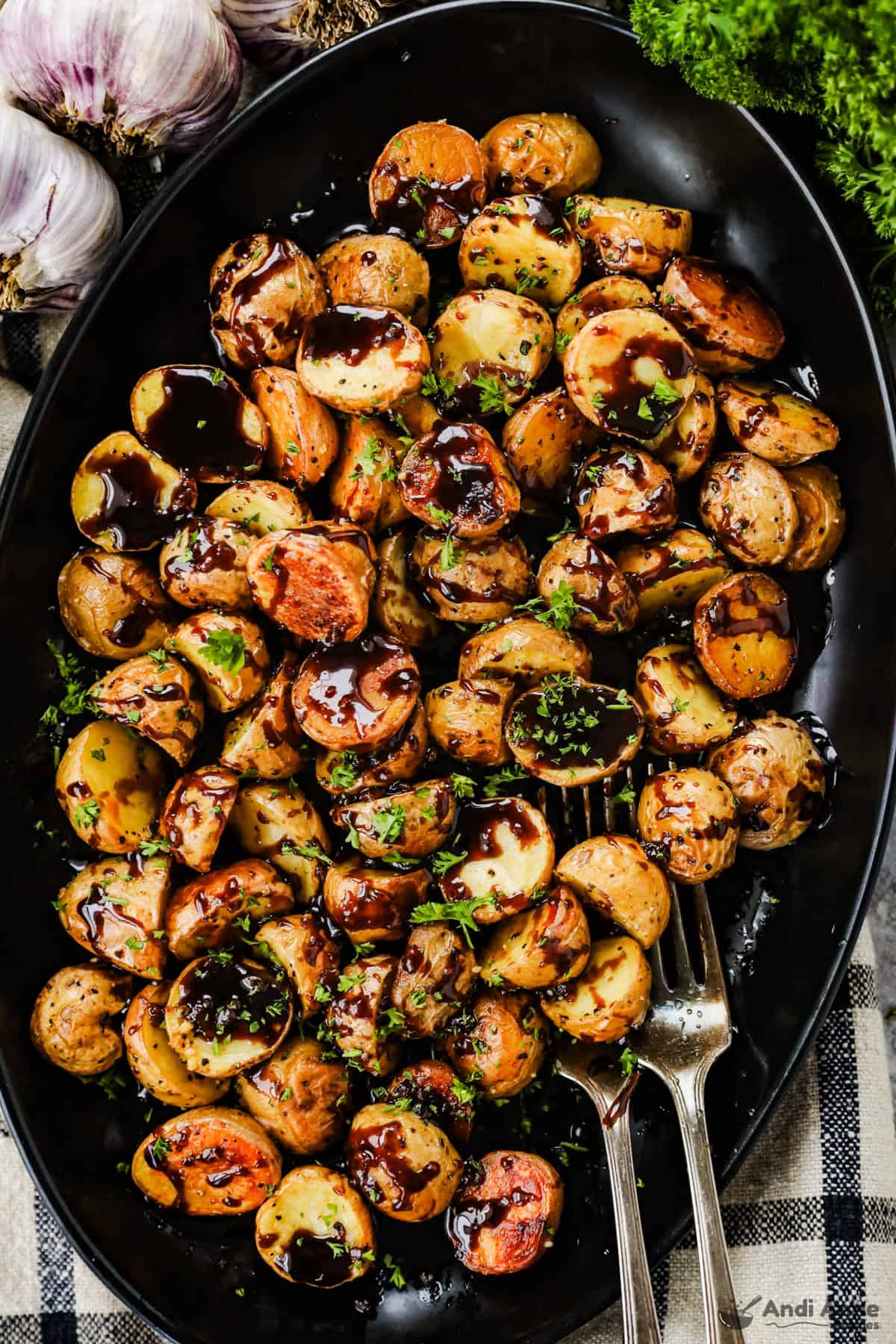 A large black serving dish with honey balsamic roasted baby potatoes and two forks.