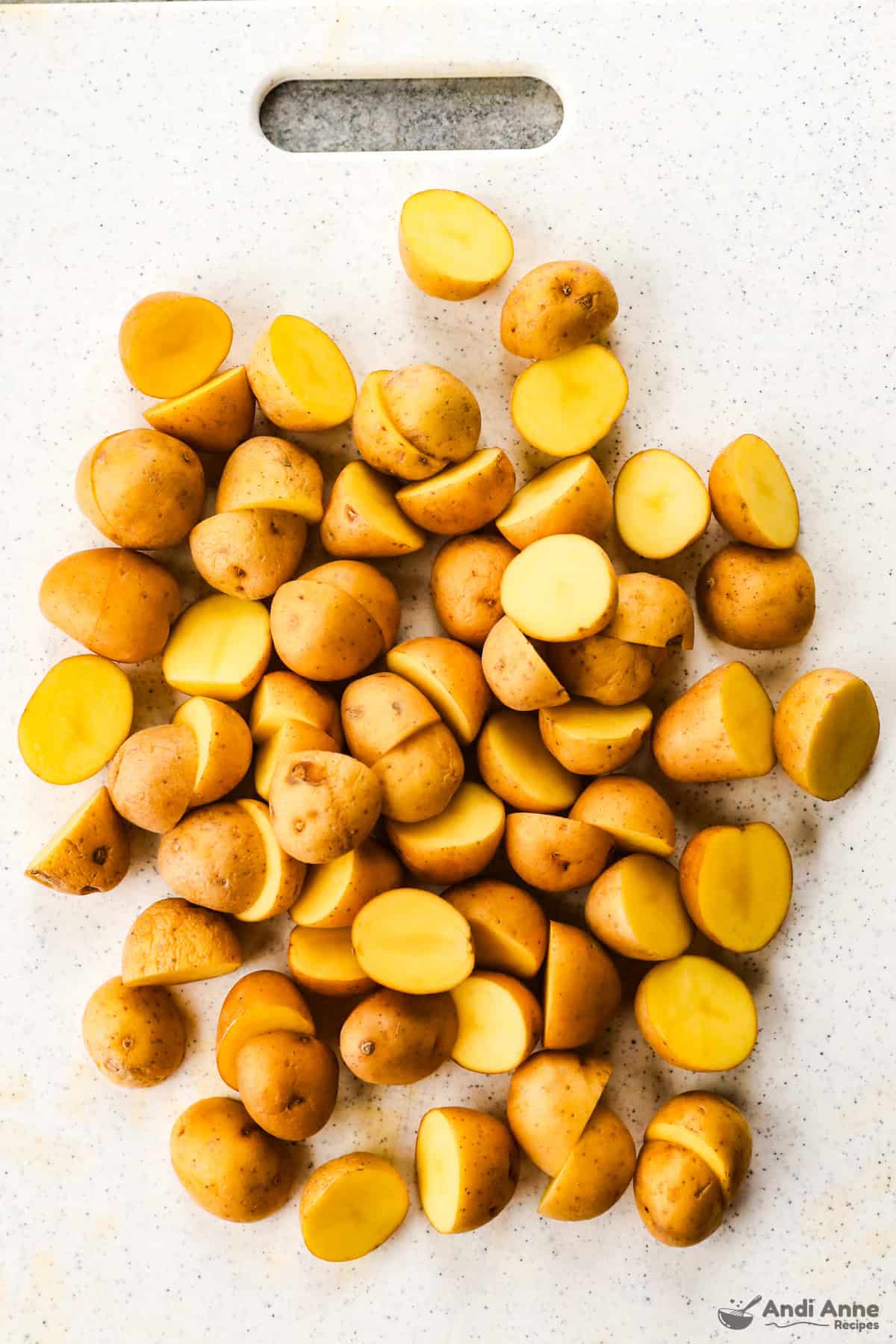 Halved baby potatoes are on a cutting board.