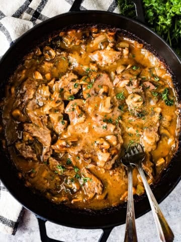 Round steak and gravy in the braising pan with two forks.