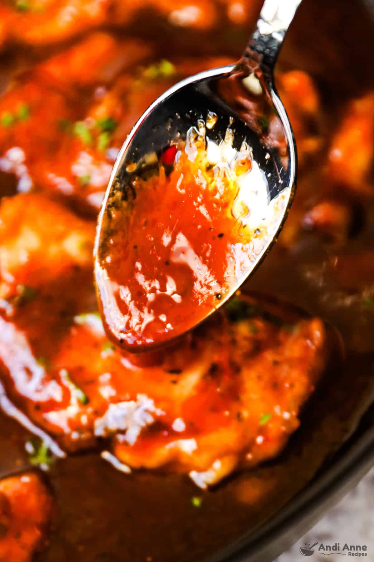 A spoon with thickened sweet and sour sauce.