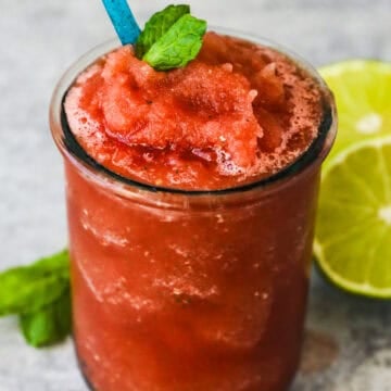 Watermelon slushie in a glass with a straw and topped with a mint leaf.