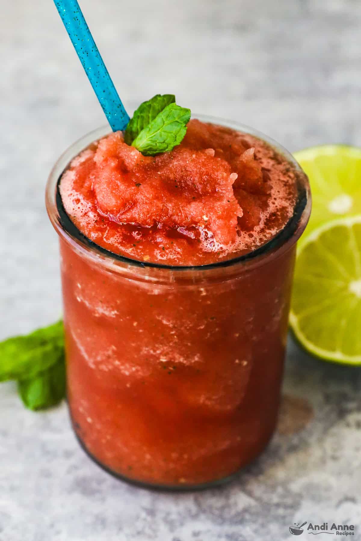 Watermelon slushie in a glass with a straw and topped with a mint leaf.