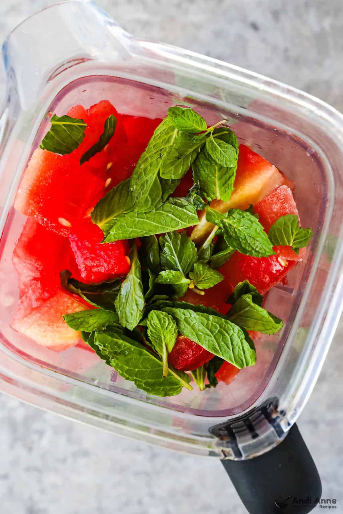 A blender with cubes of frozen watermelon and mint leaves.