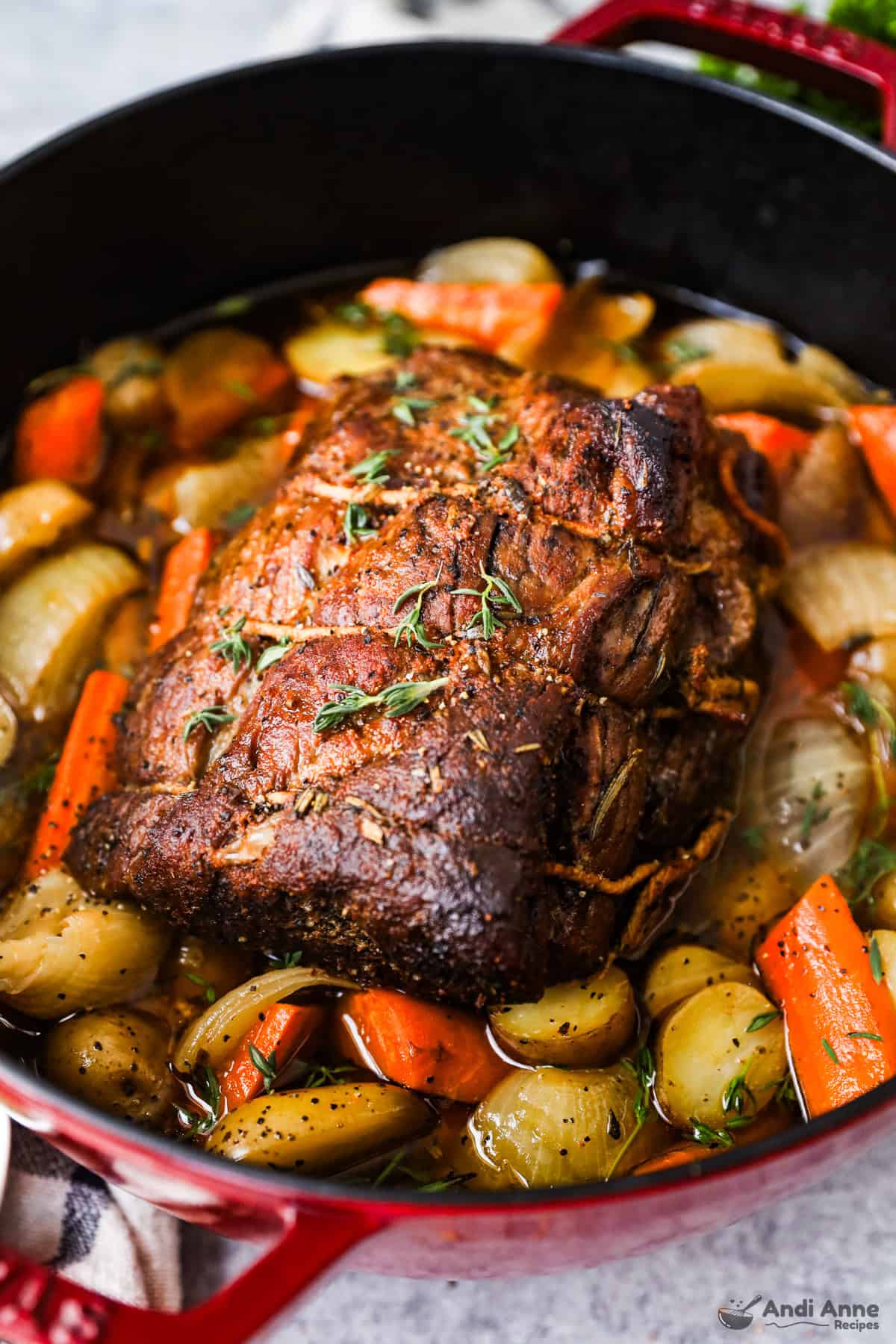A Dutch oven with a pot roast on a bed of baby potatoes, chunks of carrots, and onions.