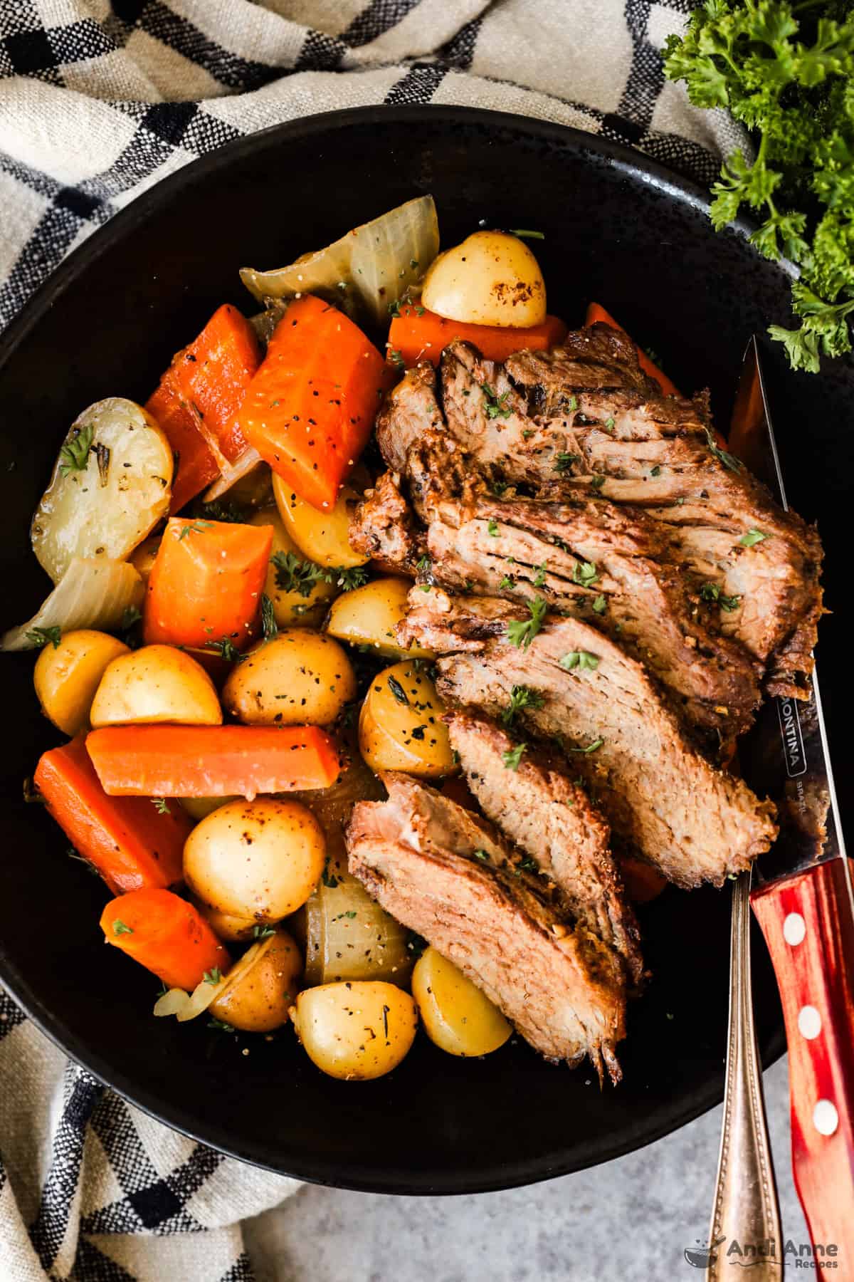 Slices of tender pot roast on a plate with baby potatoes, carrots, and onions.