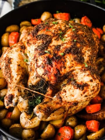 A whole roasted chicken on a bed of baby potatoes and carrot pieces in a Dutch oven.